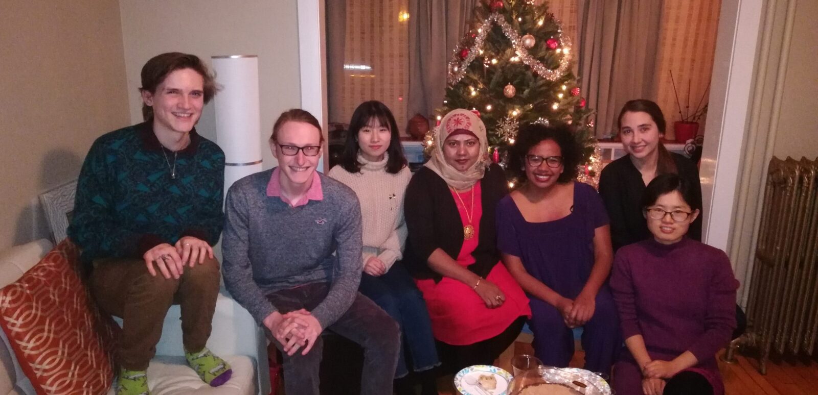 Professor and 6 lab members posing for a photo in living room in front of a Christmas tree